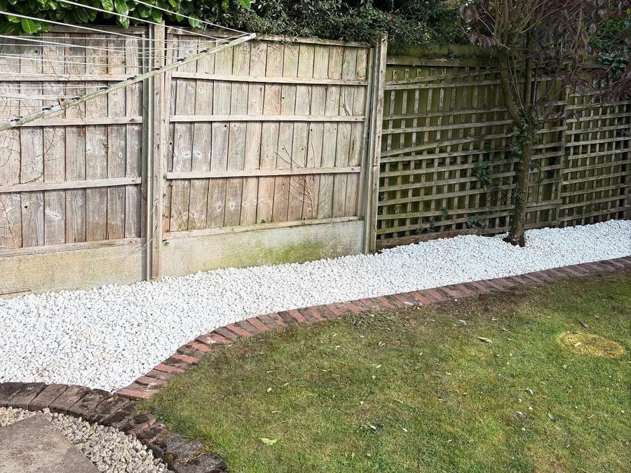 The same edge cleared, a new gravel path laid along the fence